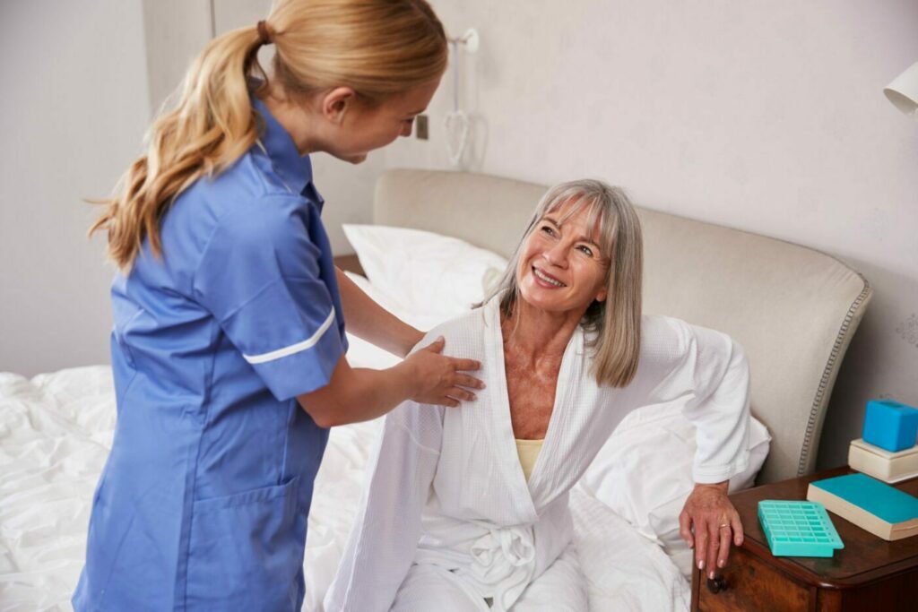 Nurse helping senior woman out of bed on home visi 2021 08 26 16 13 49 utc scaled e1662562377425