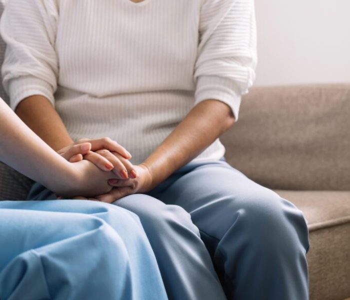 Happy patient is holding caregiver for a hand while spending time together. Elderly woman in nursing home and nurse.